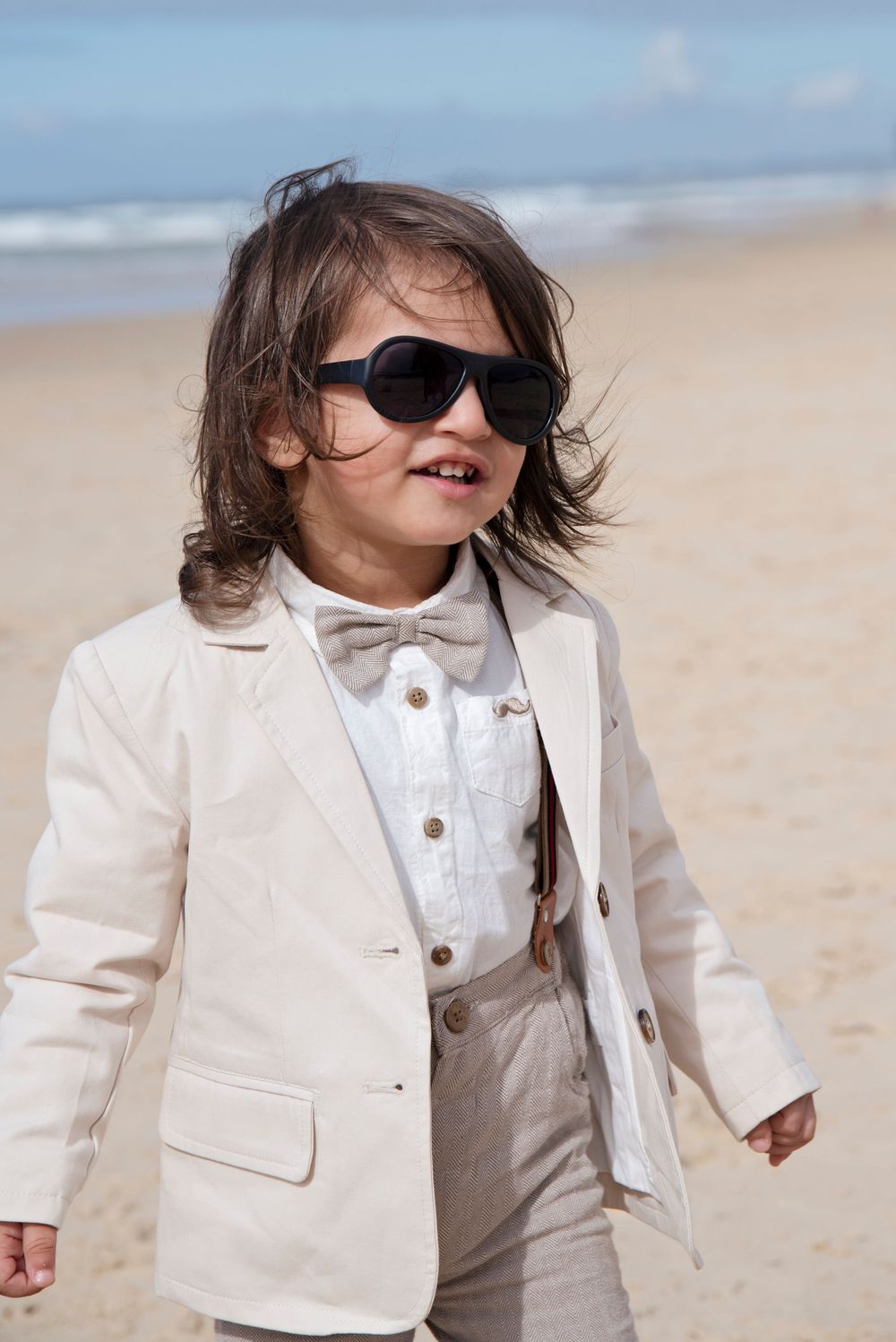 little 2yr old boy with a cream suit and sunglasses on Gold Coast beach