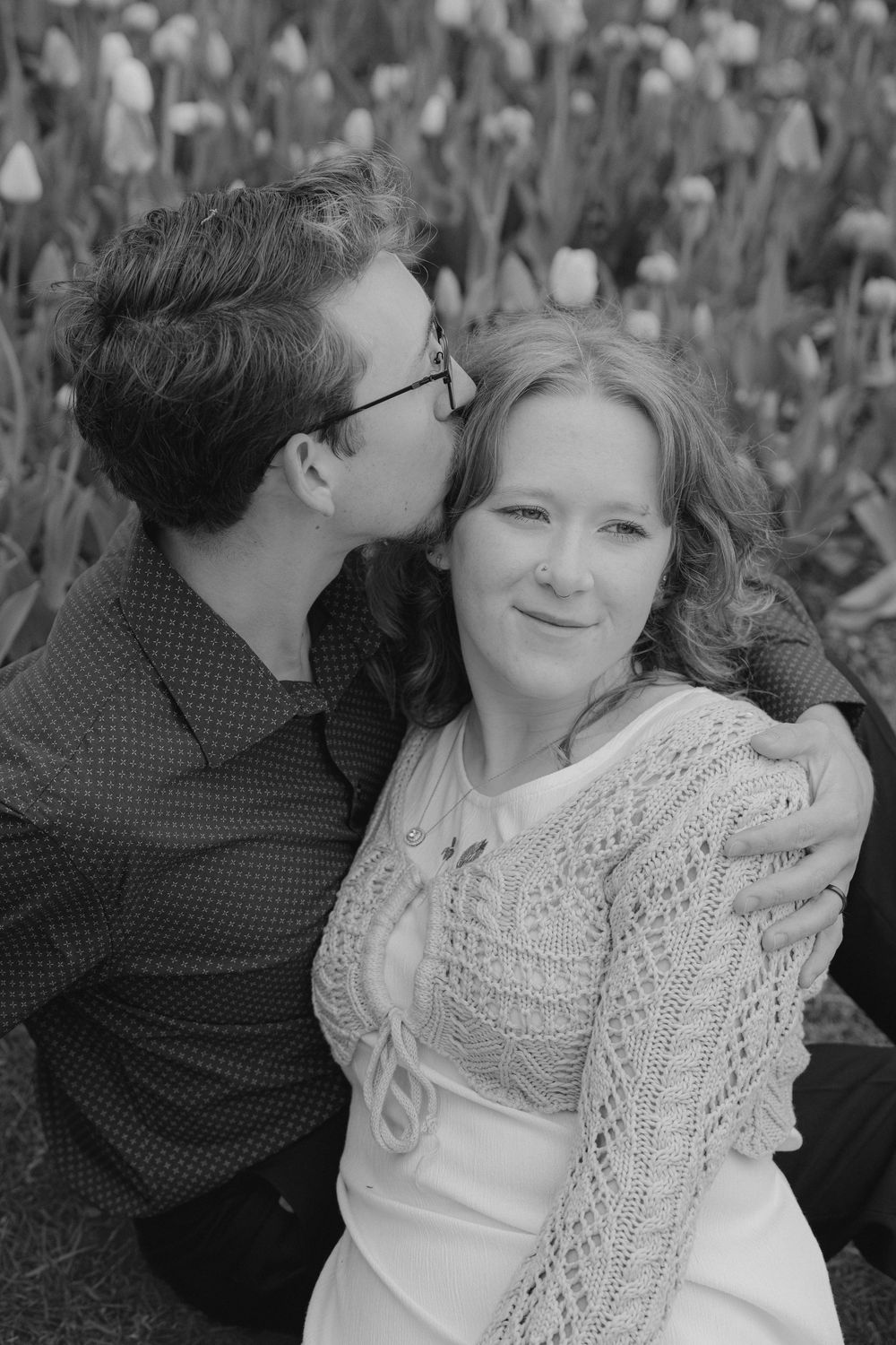 A black and white intimate portrait of a couple among flowers.