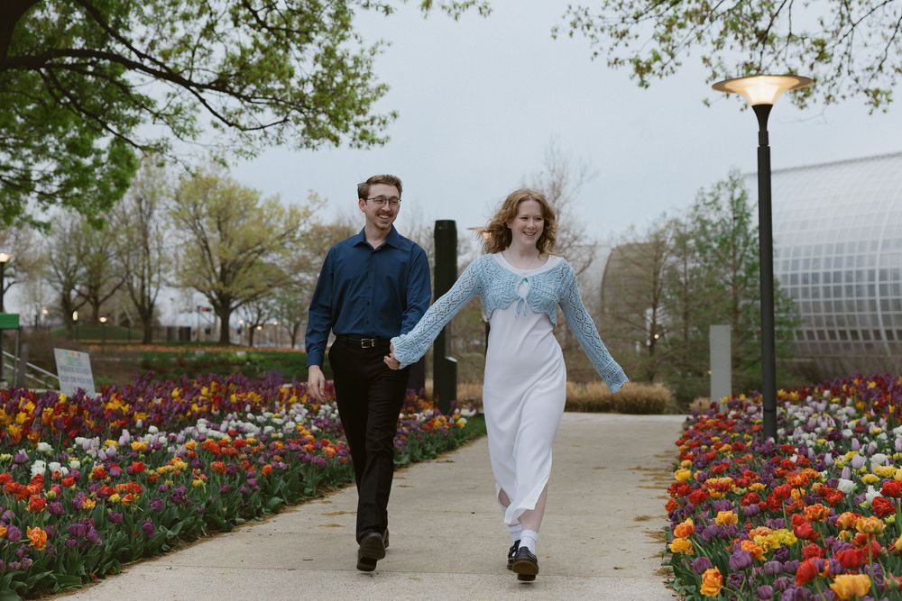 Couple walking hand in hand along pathway surrounded by colorful tulip garden.