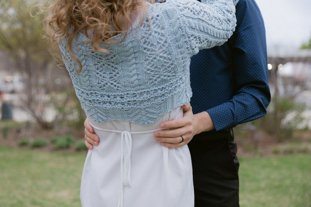 A romantic embrace in a garden setting showing a light blue knit sweater and white dress.