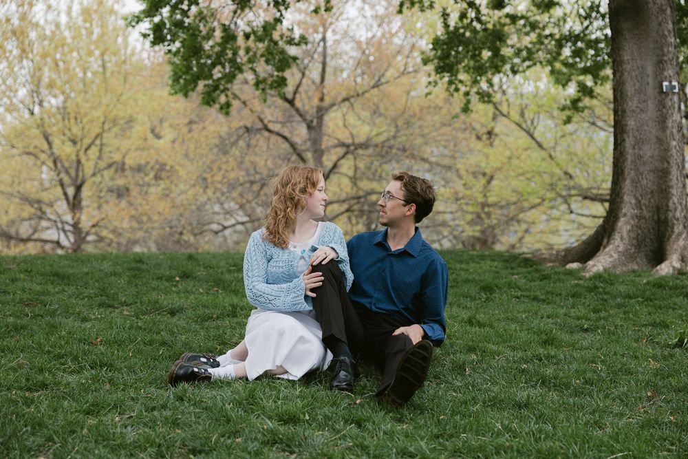 Couple sitting on grass with their dog in a park setting.