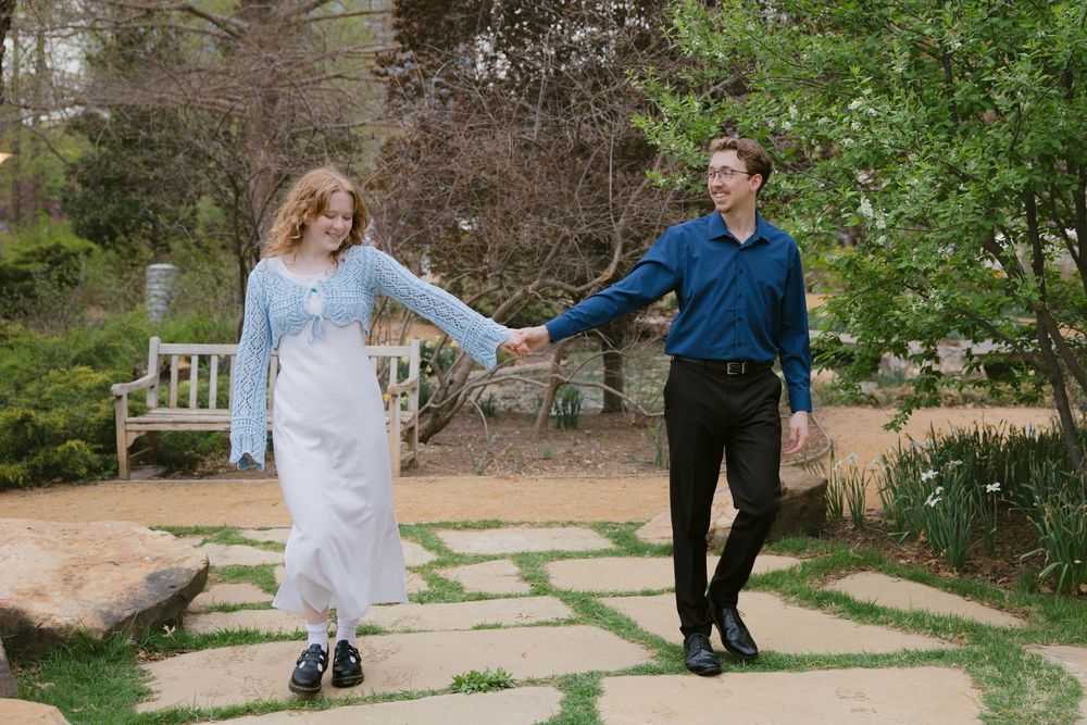 A couple walking hand in hand along a stone path in a garden setting.