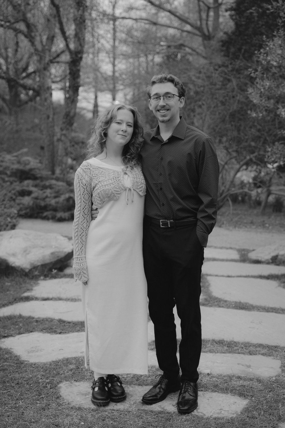 A black and white portrait of a couple standing on a stone pathway.
