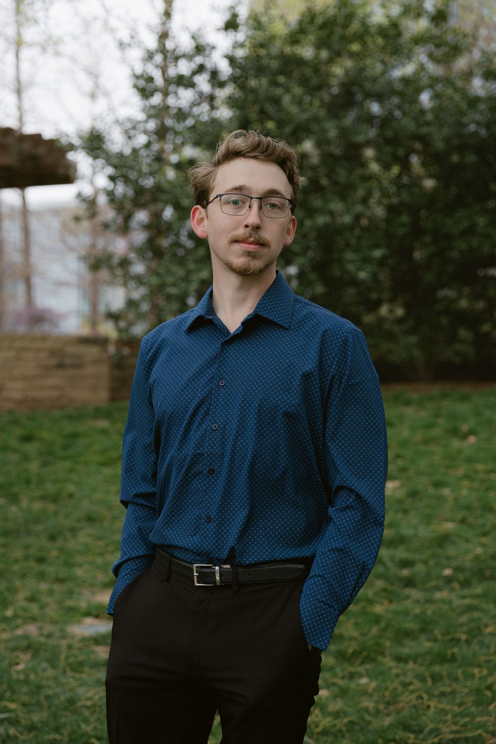 A person in a navy blue button-down shirt and dark pants standing outdoors.