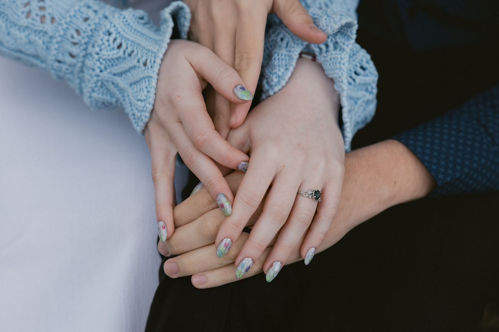 Close-up of hands showing off engagement ring with blue lace sleeve detail.