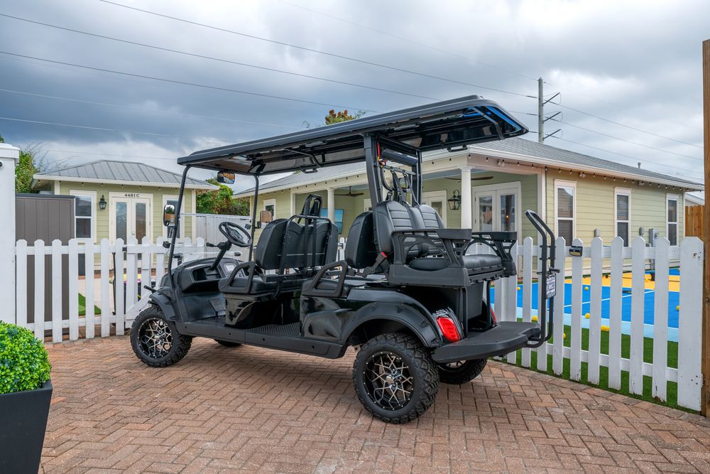 A lifted black pickup truck with custom wheels and off-road modifications parked in front of a white picket fence.
