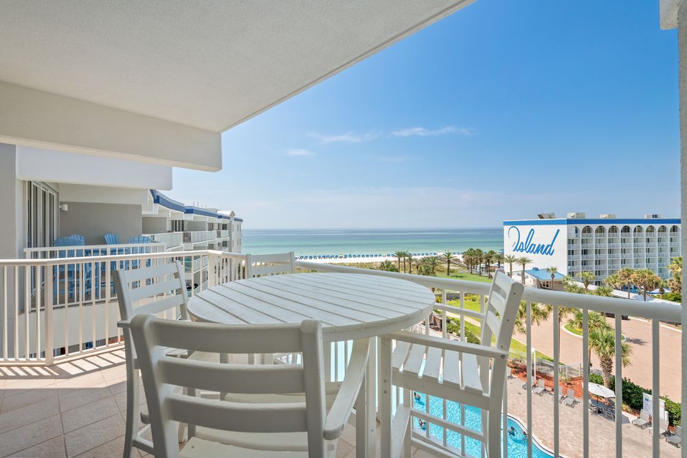 Ocean view balcony of beachfront hotel with white lounge chairs and palm trees in the distance.