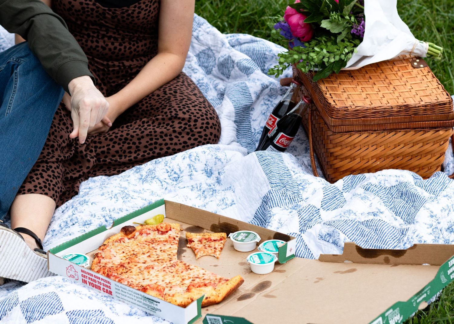 A picnic spread with wicker baskets and food items laid out on a blanket in the grass.