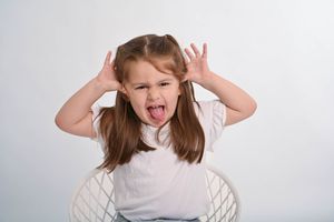 Person in white top making silly faces and hand gestures against white background.