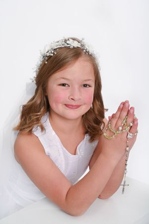 Person in white dress with floral headpiece holding rosary beads in prayer pose.