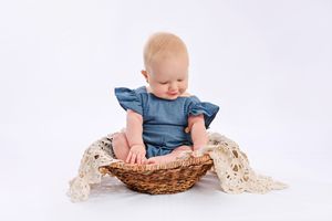 Baby exploring wicker basket with lace details in studio setting.