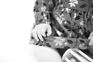Black and white detail shot of small hands in a floral dress with decorative elements.