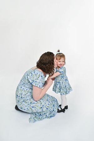 Mother and child in matching floral dresses sharing a tender moment on white background.