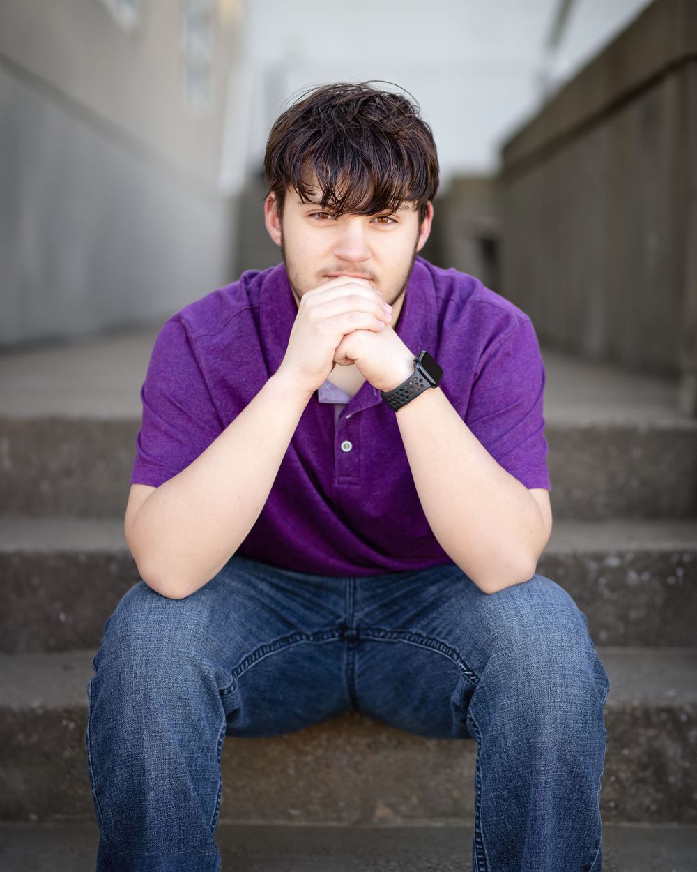 Person in purple polo shirt sits thoughtfully on concrete steps.