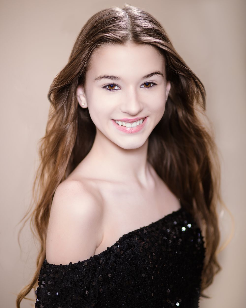 Portrait of someone with long brown hair wearing a sparkly black off-shoulder top against a neutral background.