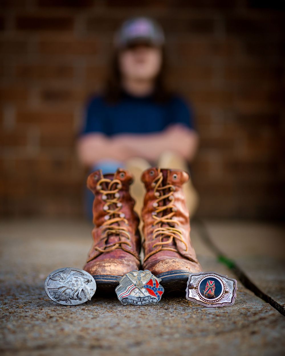 Worn brown leather boots with vintage belt buckles arranged on concrete surface.