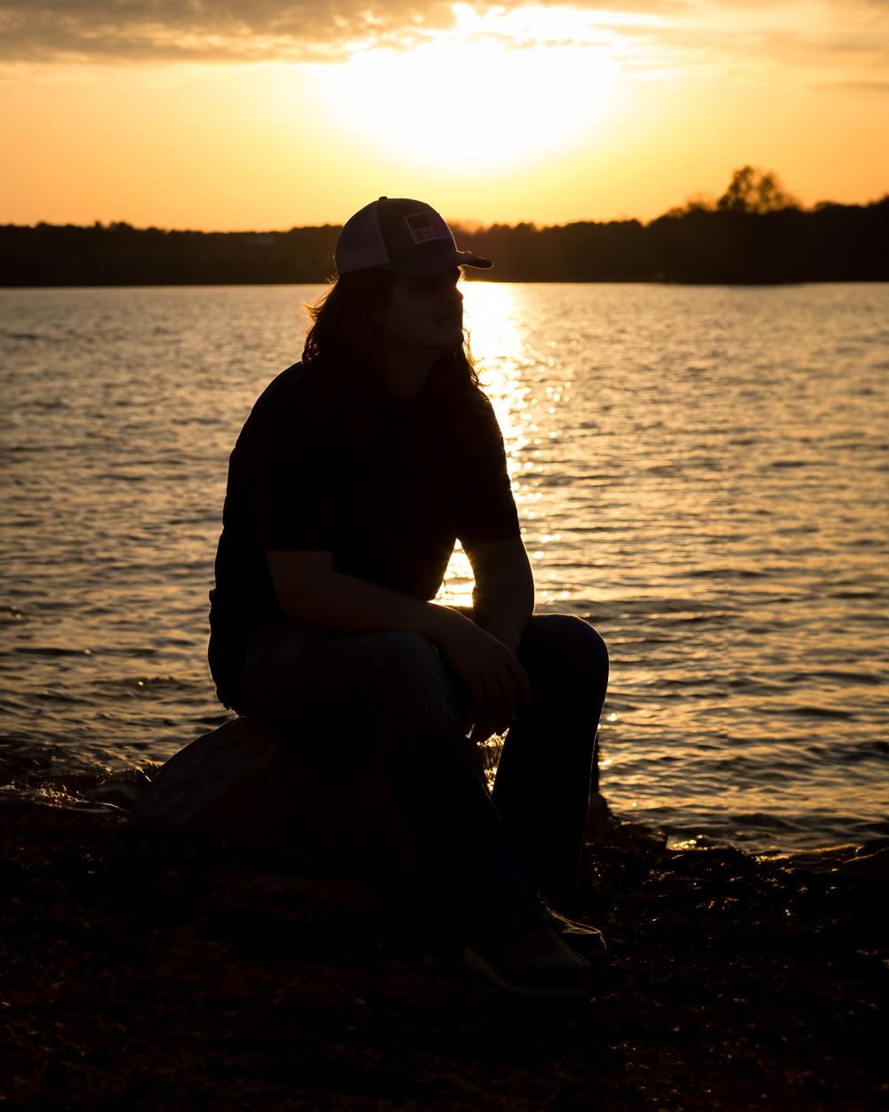 A silhouette sits peacefully by the water during a golden sunset.