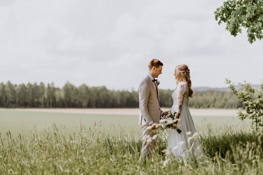 Brudpar står vid en äng och fotograferas av Fotograf Veronica Eng under ett bröllop i Örebro.