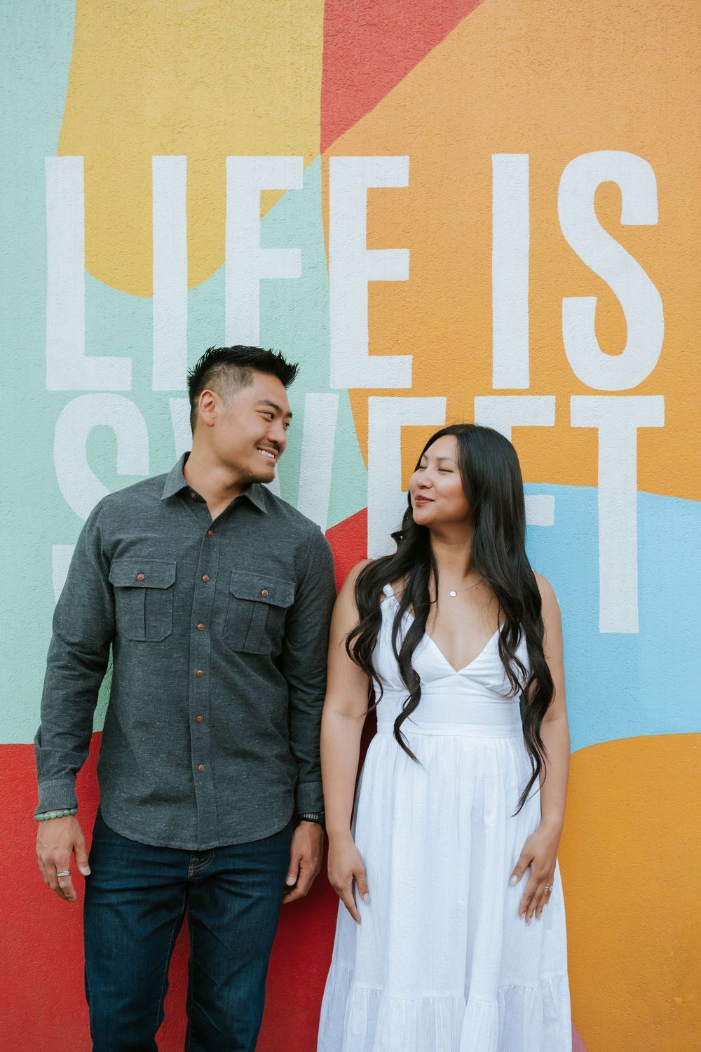 A couple shares playful moments against a colorful geometric wall mural with pastel and bright tones.