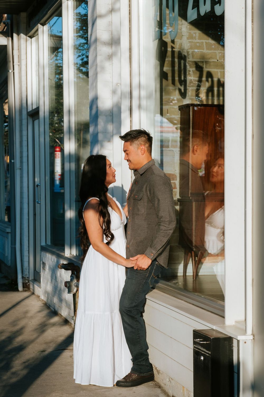 A couple shares an intimate moment outside a storefront window on a sunny afternoon.