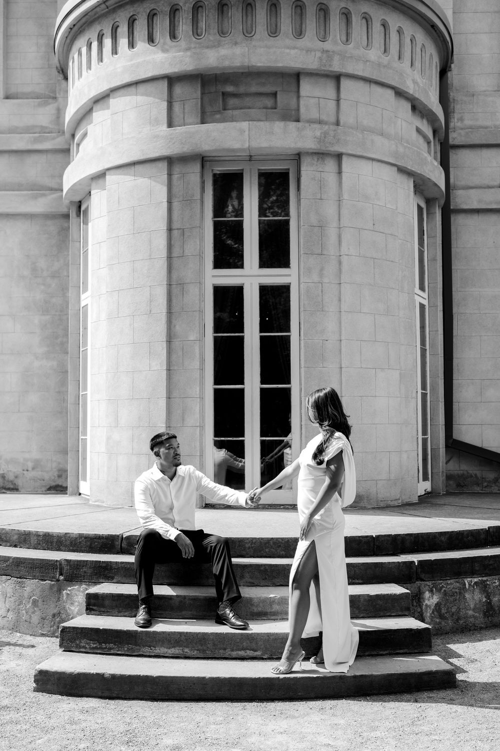 Black and white photo of a couple holding hands on elegant stone steps outside a classic European building.