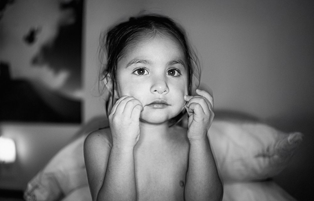 Black and white portrait of a young girl resting her chin on her hands with a thoughtful expression.