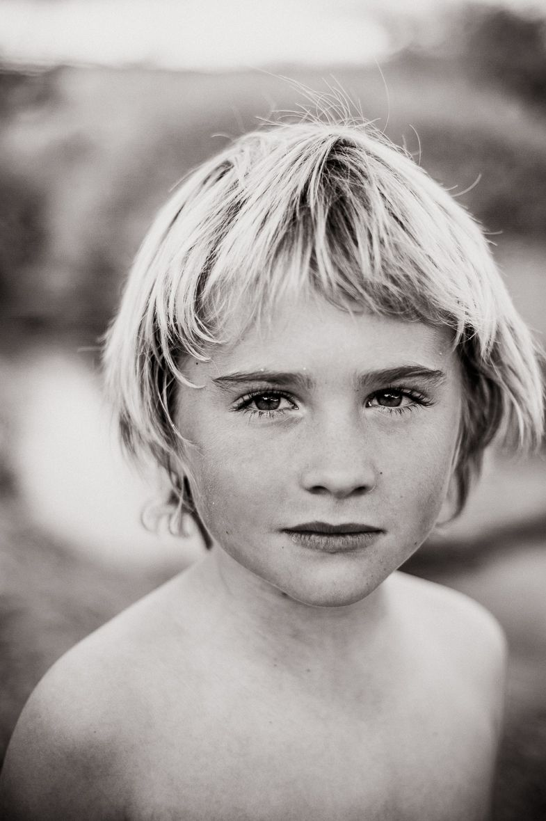 Black and white portrait of a young child with blonde hair, freckles, and expressive eyes gazing at the camera.