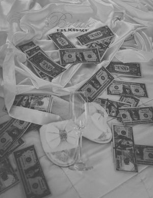 Black and white photograph showing scattered US dollar bills on a crumpled white surface.