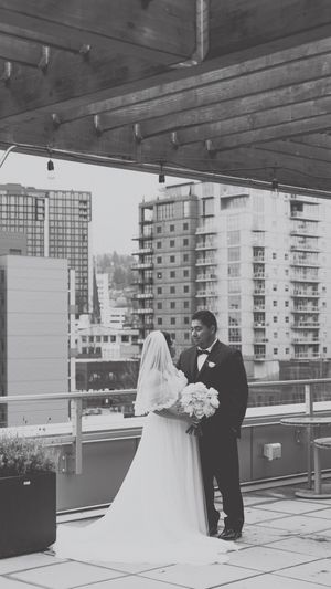 Black and white wedding photos show a romantic rooftop first look moment with city buildings in the background.