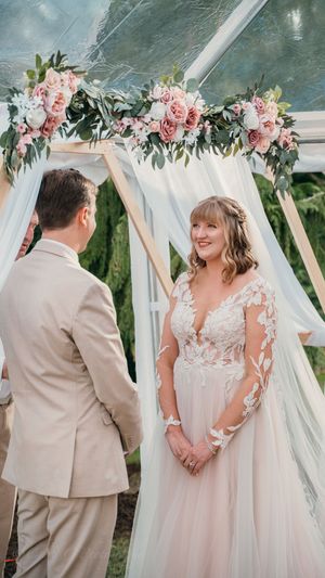 A romantic wedding ceremony under a white canopy decorated with pink roses and eucalyptus garland.