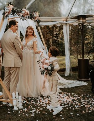 Romantic outdoor wedding ceremony under white draped canopy with scattered rose petals and floral arrangements.