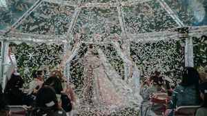 A panoramic view of a wedding celebration with guests under a tent structure with hanging lights and decor.