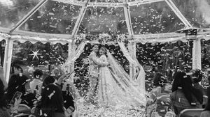 A black and white panoramic shot of a wedding reception with guests gathered under a large tent structure.