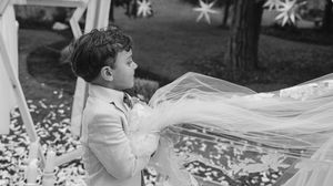 A black and white photograph shows a child playing with flowing white fabric in a garden setting.
