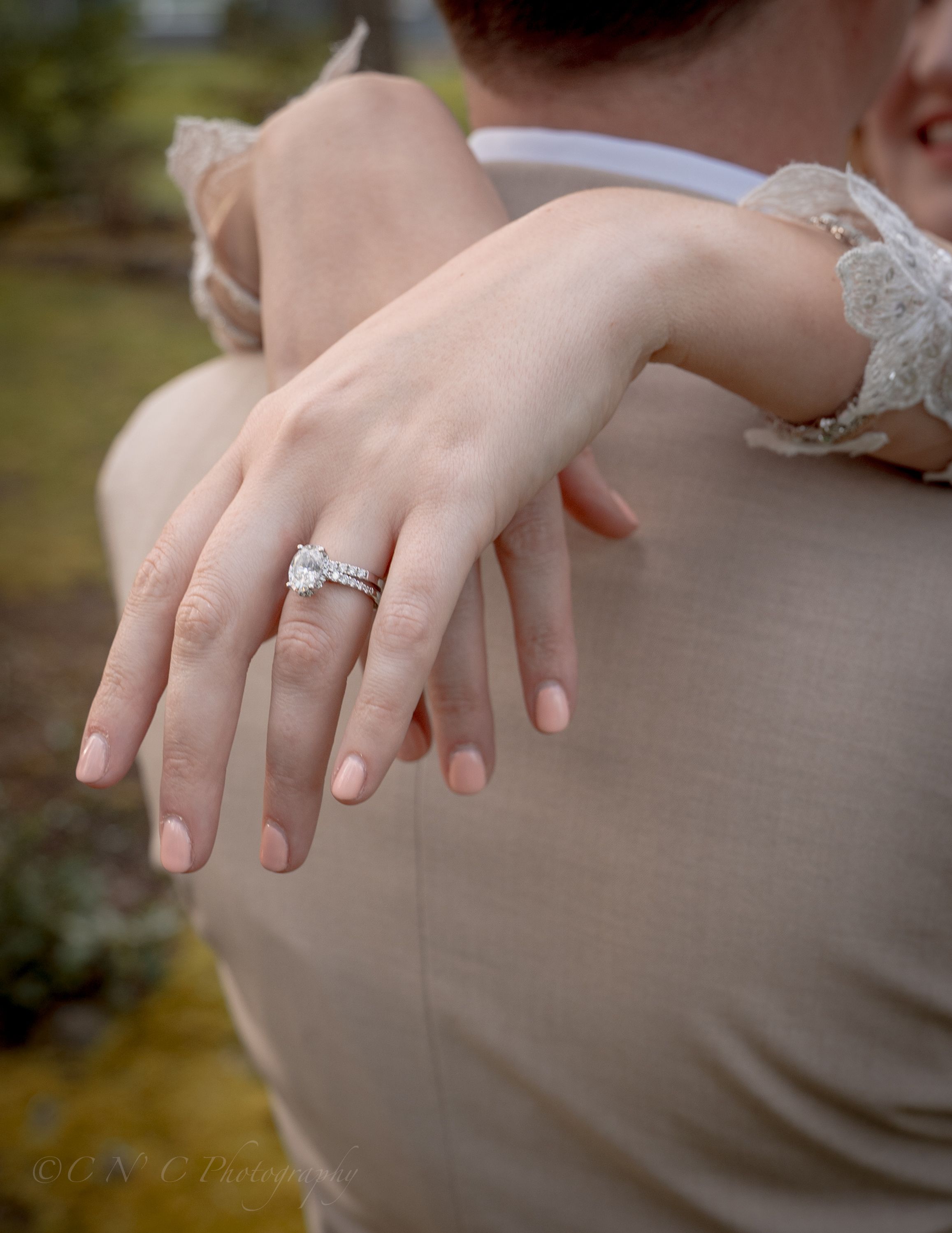 Close-up of an engagement ring on a hand resting against a neutral colored surface.