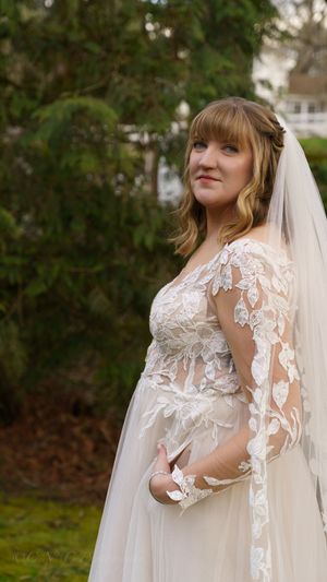 Elegant lace wedding gown with sheer long sleeves and delicate floral appliques shown in outdoor garden setting.