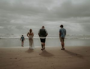 A group of people walking along a misty beach shoreline under an overcast sky.