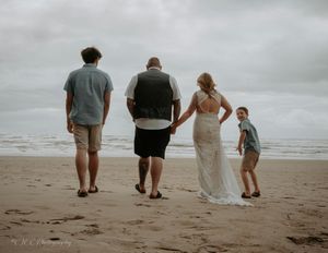 Four people walking along a misty beach shoreline in casual attire on an overcast day.