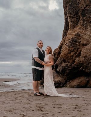 A couple shares an intimate moment on a cloudy beach with dramatic rock formations in the background.