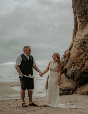 A couple shares a romantic moment on a cloudy beach with dramatic cliffs in the background.