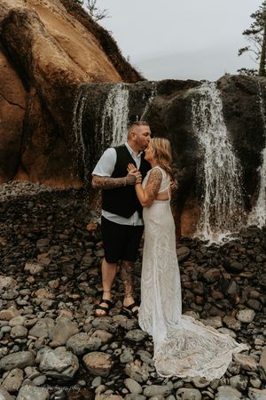 A romantic couple shares intimate moments near a cascading waterfall against a rocky landscape.