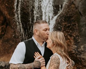 A romantic couple embraces and kisses in a rustic outdoor setting with autumn colors and natural scenery.