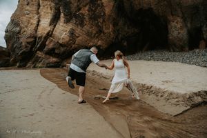 Couple walking and dancing together on a sandy beach near rocky cliffs.
