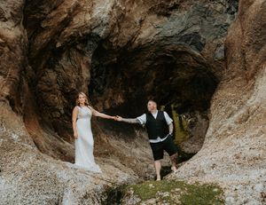 A couple explores a scenic rocky cave formation along a rugged coastline during a photo session.