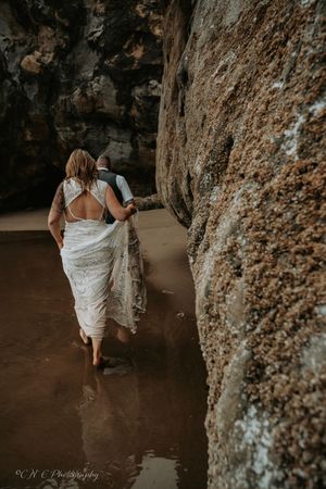 A person in a white dress walks barefoot through shallow water along a rocky canyon wall in moody lighting.