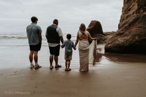 A family silhouette walking together along a misty beach with cliffs in the background.