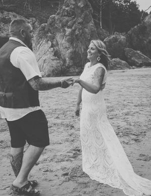 A black and white photo of a couple holding hands on a scenic beach near rocky cliffs.