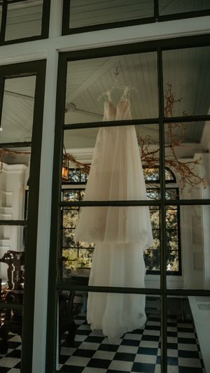 White wedding dress hanging in a sunlit room with black and white checkered floors.