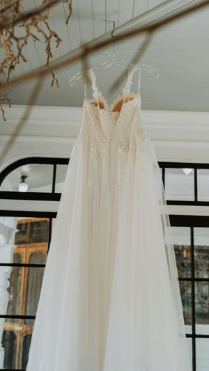 Multiple elegant white wedding dresses displayed in a bright room with large windows.