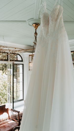 Elegant white wedding dresses hanging from ceiling fixtures in a bright sunlit room.